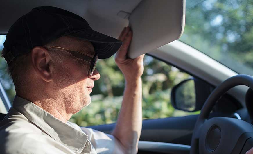 Mann mit kopfbedeckung schützt sich im auto vor der sonne mit der sonnenblende